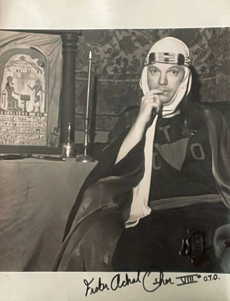 Frater Achad Osher VIII OTO (J. Edward "Jerry" Cornelius) as Saladin making the sign of Silence. Background: Stele of Revealing and candles